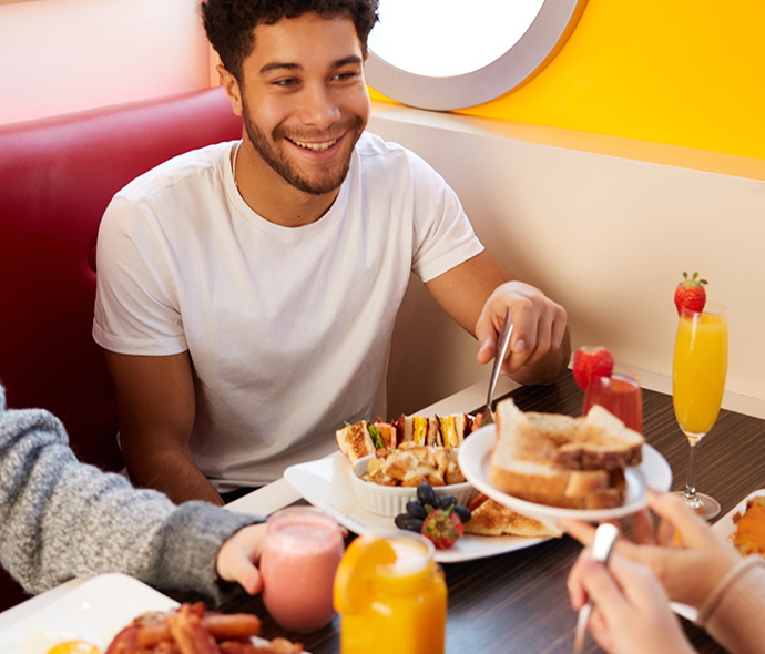 Un groupe d’amis partageant un brunch convivial avec des sandwichs, des fruits frais, des toasts et des boissons comme des jus et des smoothies.