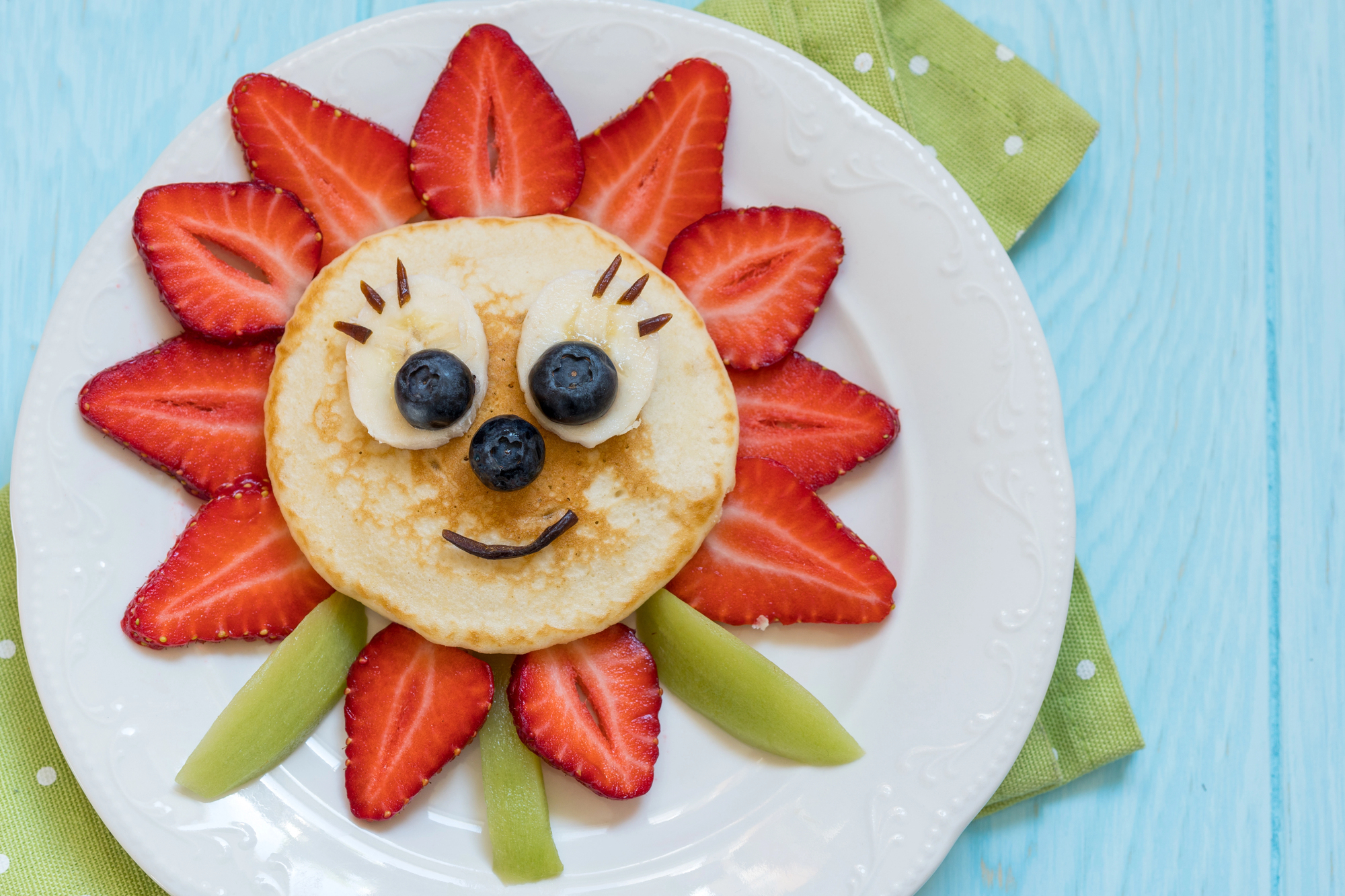 Une assiette ludique de brunch pour enfants avec un pancake décoré en forme de soleil, entouré de fruits frais. Pourquoi le brunch en famille est une tradition à adopter ? C’est une occasion idéale pour éveiller les enfants aux plaisirs d’une alimentation saine et amusante.