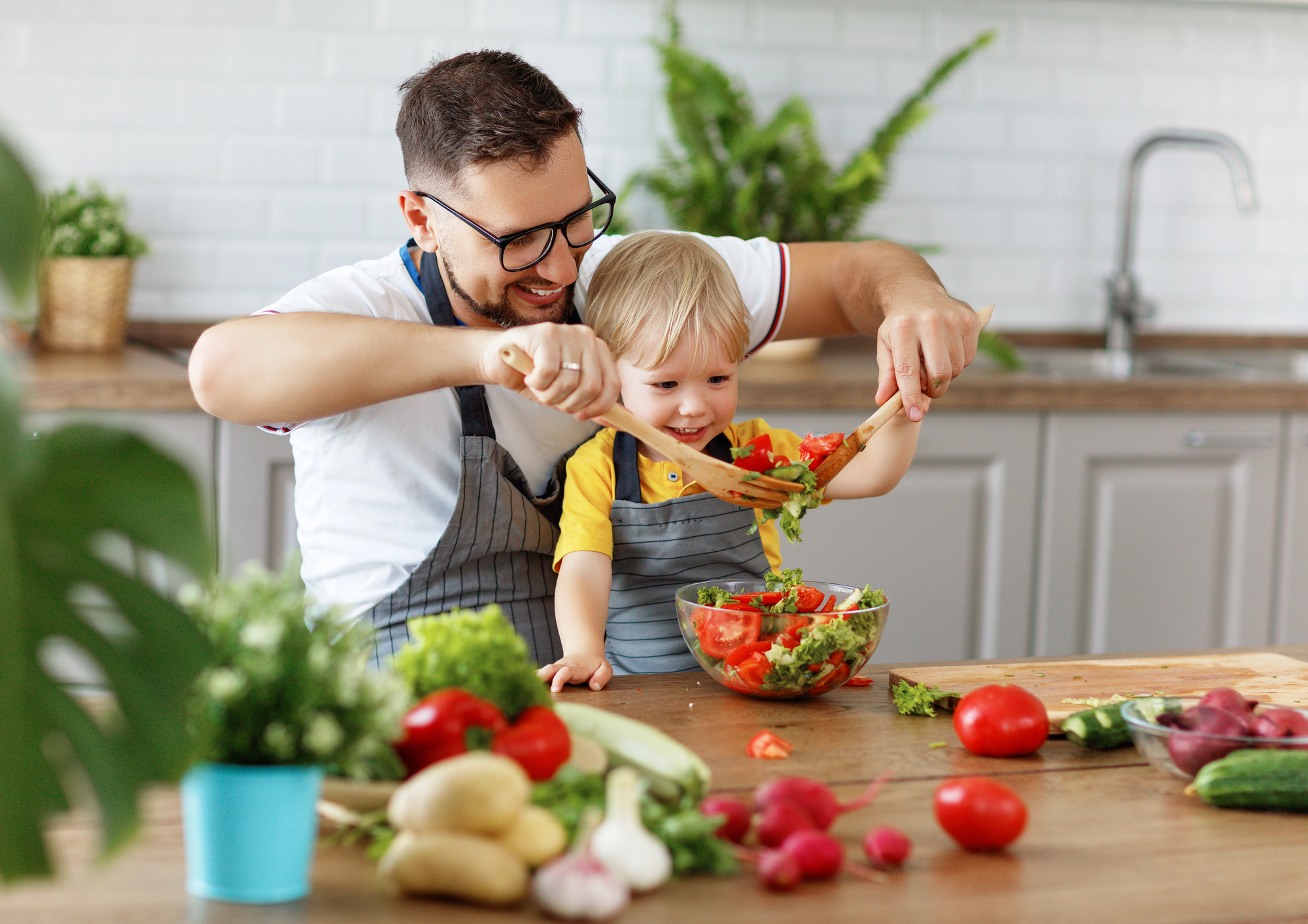 Un père et son fils préparent une salade fraîche pour un brunch familial, partageant un moment complice en cuisine. Pourquoi le brunch en famille est une tradition à adopter ? Cuisiner ensemble renforce les liens et éduque les enfants à l’importance d’une alimentation équilibrée.