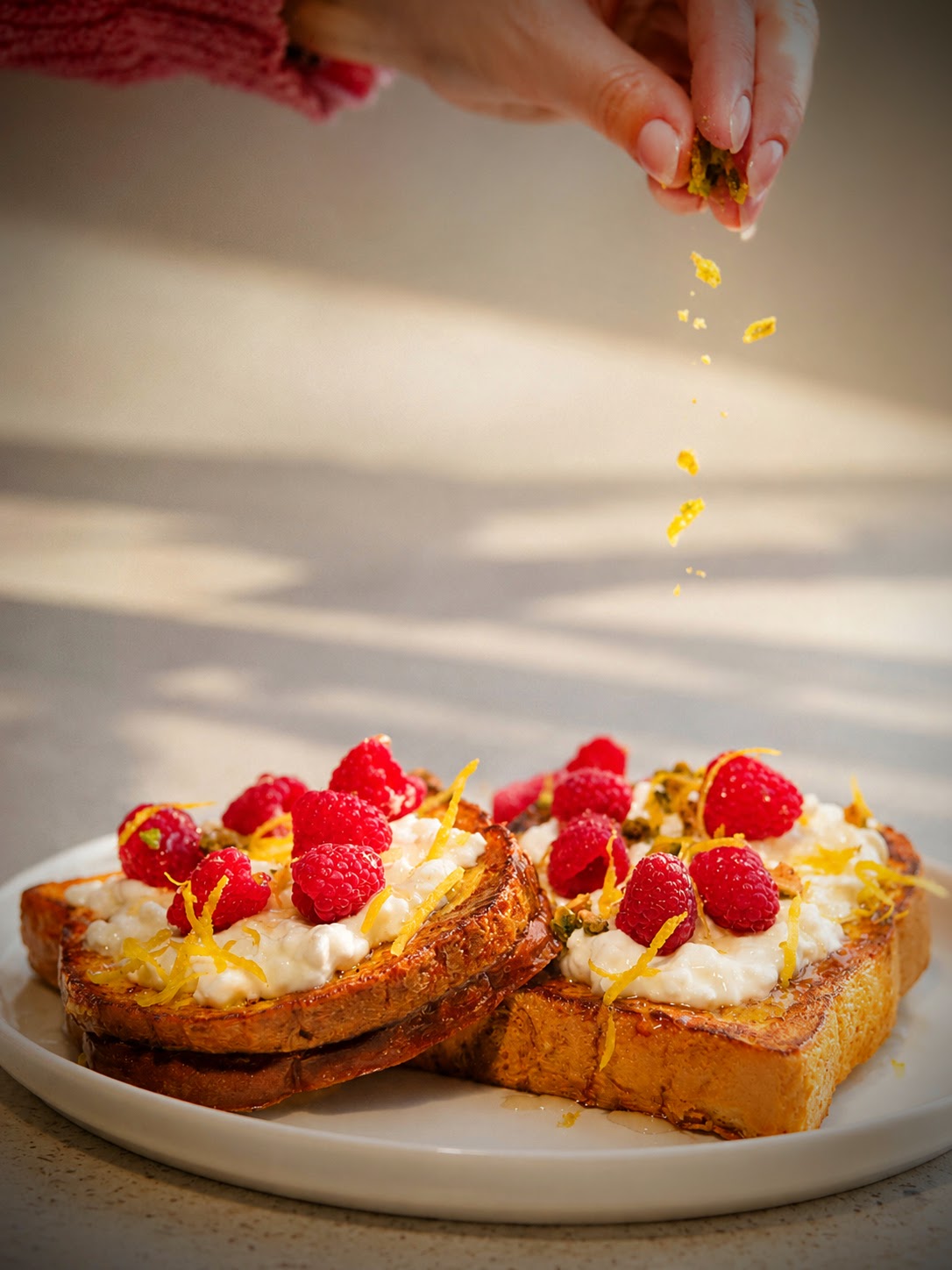 Main ajoutant du zeste sur du pain doré garni de framboises et crème, pour un brunch gourmand équilibré avec une touche fruitée