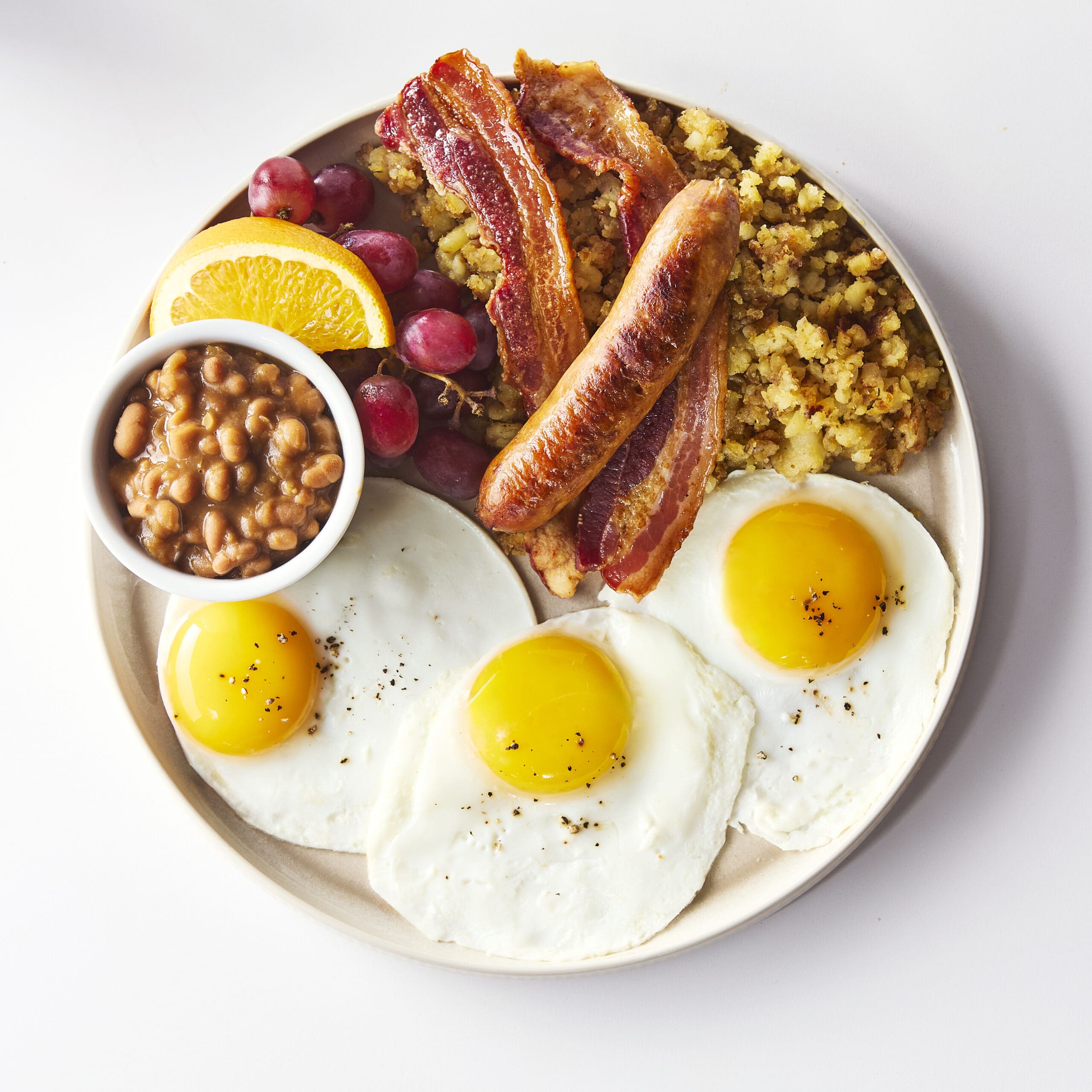 Le « Cocolossal Brunch » d'Allô mon Coco, avec trois œufs, des haricots blancs, des pommes de terre, des fruits, du bacon en tranches épaisses et des saucisses artisanales.